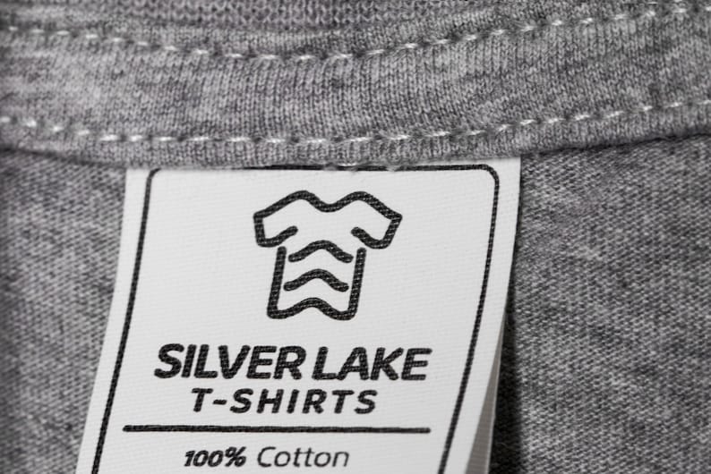 May include: A white tag with black text and a graphic of a t-shirt. The tag reads "Silver Lake T-Shirts 100% Cotton".