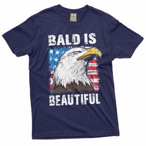 May include: A navy blue t-shirt with a distressed white graphic of a bald eagle with an American flag background. The text "Bald is Beautiful" is printed in white below the eagle.