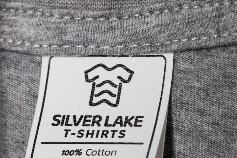 May include: A white tag with black text and a graphic of a t-shirt. The tag reads "Silver Lake T-Shirts 100% Cotton".