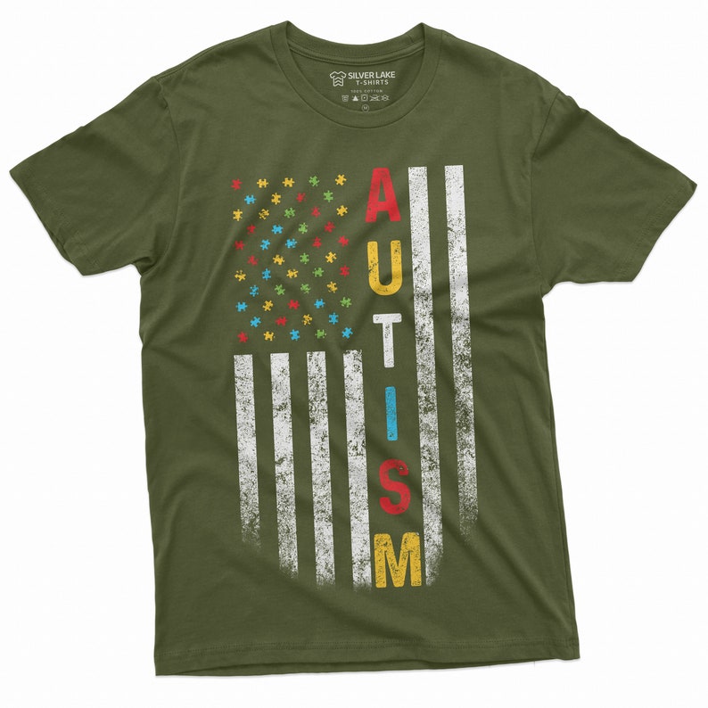 Peut inclure: T-shirt vert olive avec un motif de drapeau am&eacute;ricain vieilli. Les &eacute;toiles du drapeau sont remplac&eacute;es par des pi&egrave;ces de puzzle color&eacute;es, et le mot "AUTISME" est imprim&eacute; verticalement en lettres grasses. Le t-shirt est de Silver Lake T-Shirts.