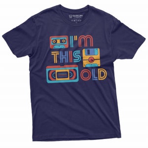 May include: A navy blue t-shirt with a retro design featuring a cassette tape, floppy disk, and VHS tape. The text "I'm This Old" is printed on the shirt.