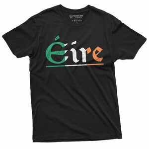 May include: Black t-shirt with a white, green, and orange graphic of the word "&Eacute;ire" in a vintage style font. The graphic includes a thin white line under the word and a faded Irish flag design.