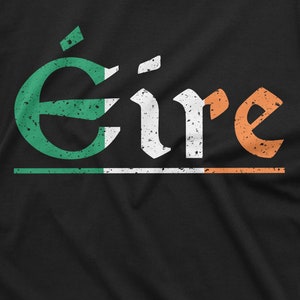 May include: A black t-shirt with a distressed white graphic of the word "&Eacute;ire" in Irish Gaelic. The graphic is layered with green, white, and orange, resembling the Irish flag.