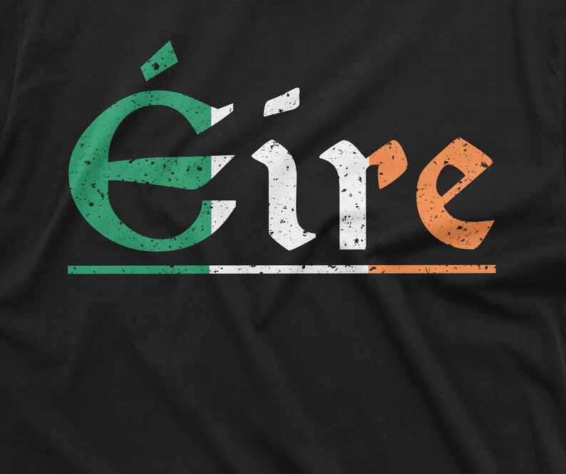 May include: A black t-shirt with a distressed white graphic of the word "&Eacute;ire" in Irish Gaelic. The graphic is layered with green, white, and orange, resembling the Irish flag.