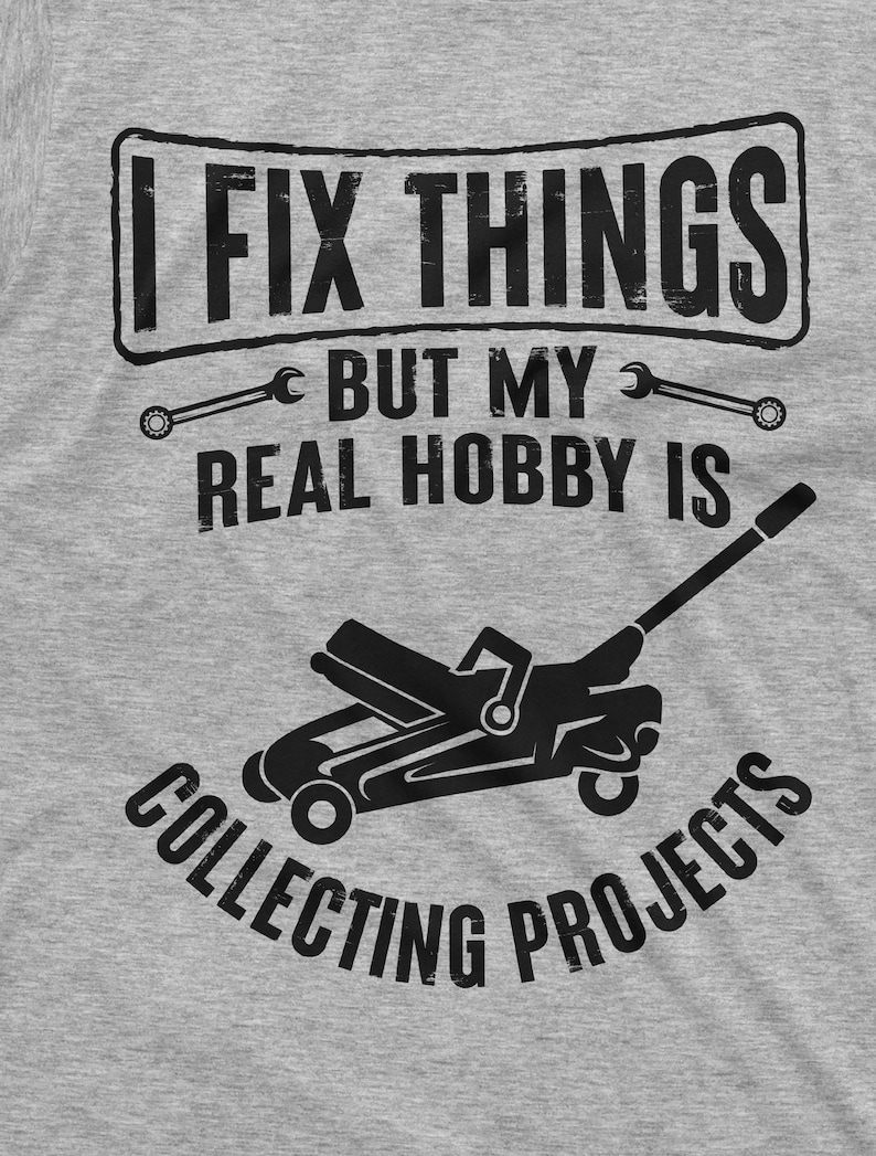 May include: A gray t-shirt with a black graphic that says "I fix things but my real hobby is collecting projects". The graphic includes two wrenches and a silhouette of a car jack.