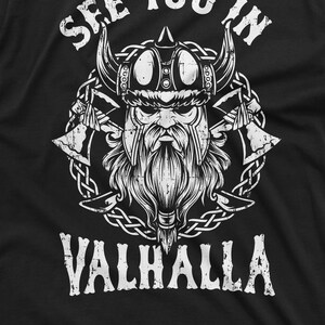 May include: Black t-shirt featuring a white graphic of a Viking with a horned helmet, long beard, and crossed axes. The text "SEE YOU IN VALHALLA" is arched above and below the Viking illustration.