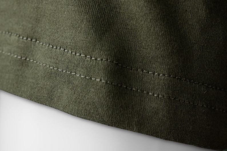 May include: Close-up of the bottom edge of a dark green garment with double stitching.