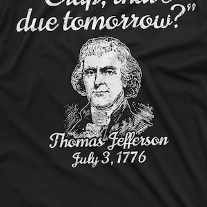 May include: A black t-shirt with a white graphic print of Thomas Jefferson with the quote "Crap, that's due tomorrow?" and the date "July 3, 1776".