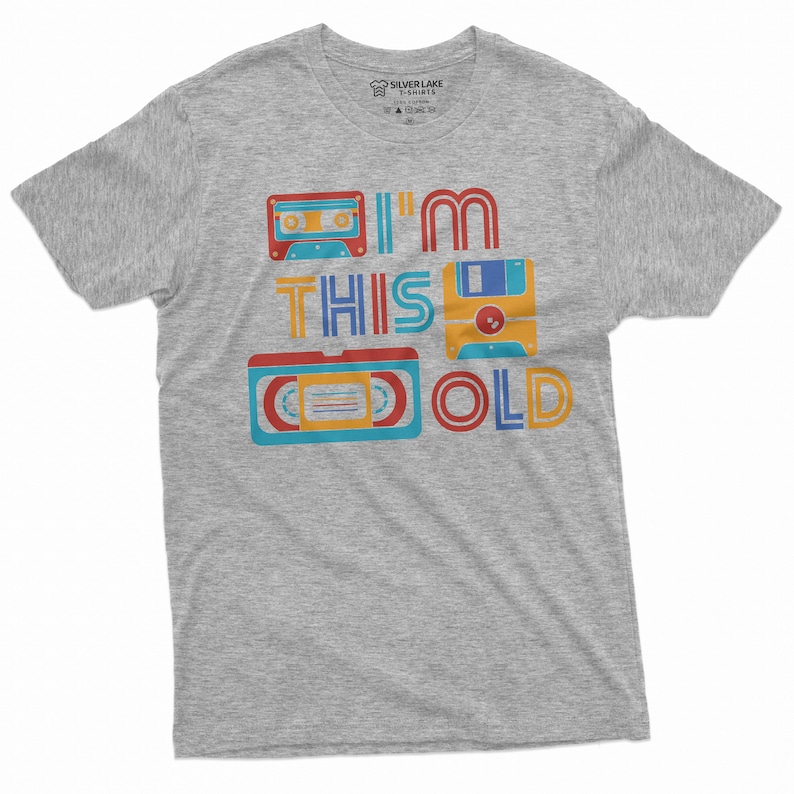 May include: A heather gray t-shirt with a retro design featuring a cassette tape, floppy disk, and VHS tape. The text on the shirt reads "I'm this old".