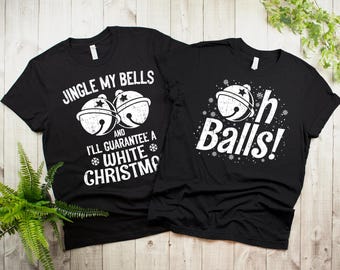 May include: Two black t-shirts with a Christmas theme. One shirt says "Jingle My Bells and I'll Guarantee a White Christmas" with a bell graphic. The other shirt says "Oh Balls!" with a bell graphic.
