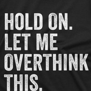 May include: Black t-shirt with white text that reads "HOLD ON. LET ME OVERTHINK THIS."