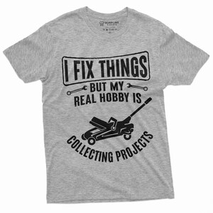 May include: Gray t-shirt with a black graphic that says "I fix things but my real hobby is collecting projects". The graphic also includes a wrench and a car jack.
