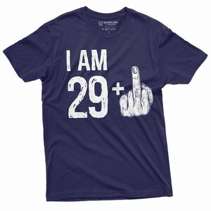 May include: Navy blue t-shirt with white text that reads "I AM 29+ " with a white middle finger graphic.