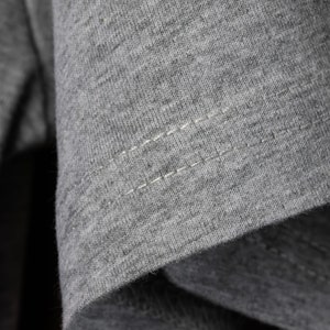 May include: Close-up of a gray t-shirt with a single row of stitching along the seam.