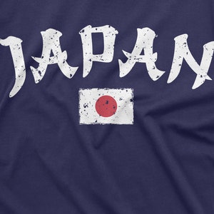 May include: A navy blue t-shirt with a white distressed graphic of the word "JAPAN" and a white distressed image of the Japanese flag with a red circle in the center.