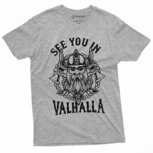 May include: A heather gray t-shirt featuring a black graphic of a Viking with a horned helmet, axes, and the text "SEE YOU IN VALHALLA." The design is centered on the front of the shirt.