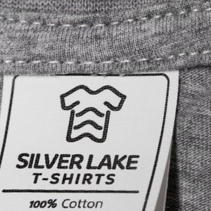 May include: A white tag with black text and a graphic of a t-shirt. The tag reads "Silver Lake T-Shirts 100% Cotton".