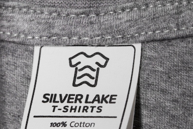 May include: A white tag with black text and a graphic of a t-shirt. The tag reads "Silver Lake T-Shirts 100% Cotton".