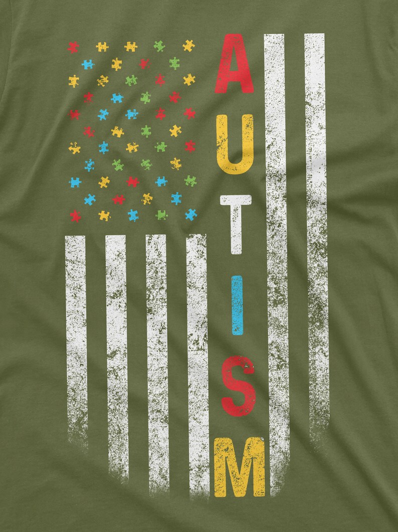Peut inclure: T-shirt vert olive avec un motif vieilli du drapeau am&eacute;ricain. Les &eacute;toiles sont remplac&eacute;es par des pi&egrave;ces de puzzle color&eacute;es, et le mot "AUTISM" est affich&eacute; verticalement. Le design a un aspect vintage et us&eacute;.