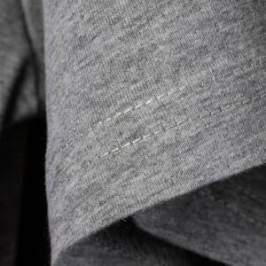 May include: Close-up of a gray t-shirt with a single row of stitching along the seam.