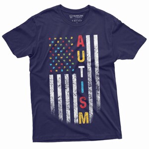 Peut inclure: T-shirt bleu marine avec un motif de drapeau am&eacute;ricain vieilli. Les &eacute;toiles sont remplac&eacute;es par des pi&egrave;ces de puzzle color&eacute;es et le mot "AUTISM" est imprim&eacute; verticalement. Le t-shirt est de Silver Lake T-Shirts.