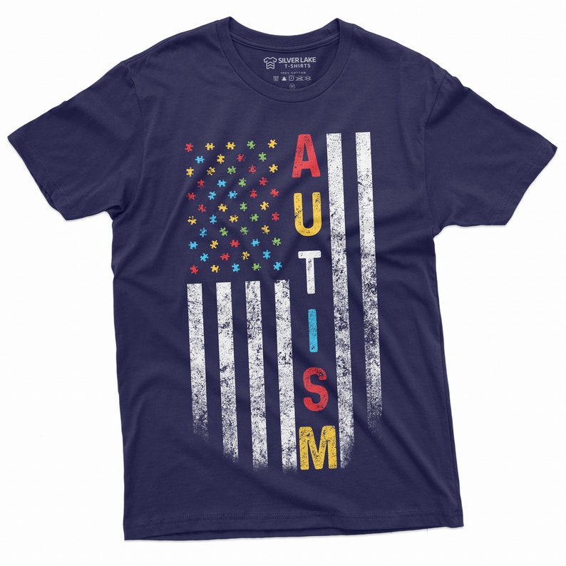 Peut inclure: T-shirt bleu marine avec un motif de drapeau am&eacute;ricain vieilli. Les &eacute;toiles sont remplac&eacute;es par des pi&egrave;ces de puzzle color&eacute;es et le mot "AUTISM" est imprim&eacute; verticalement. Le t-shirt est de Silver Lake T-Shirts.
