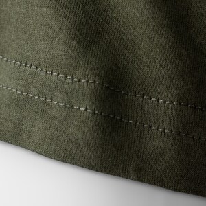 May include: Close-up of the bottom edge of a dark green garment with double stitching.