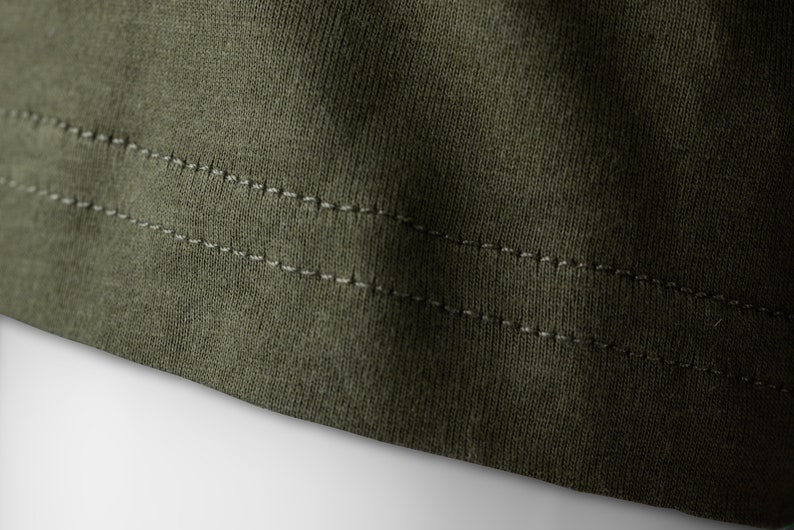 May include: Close-up of the bottom edge of a dark green garment with double stitching.