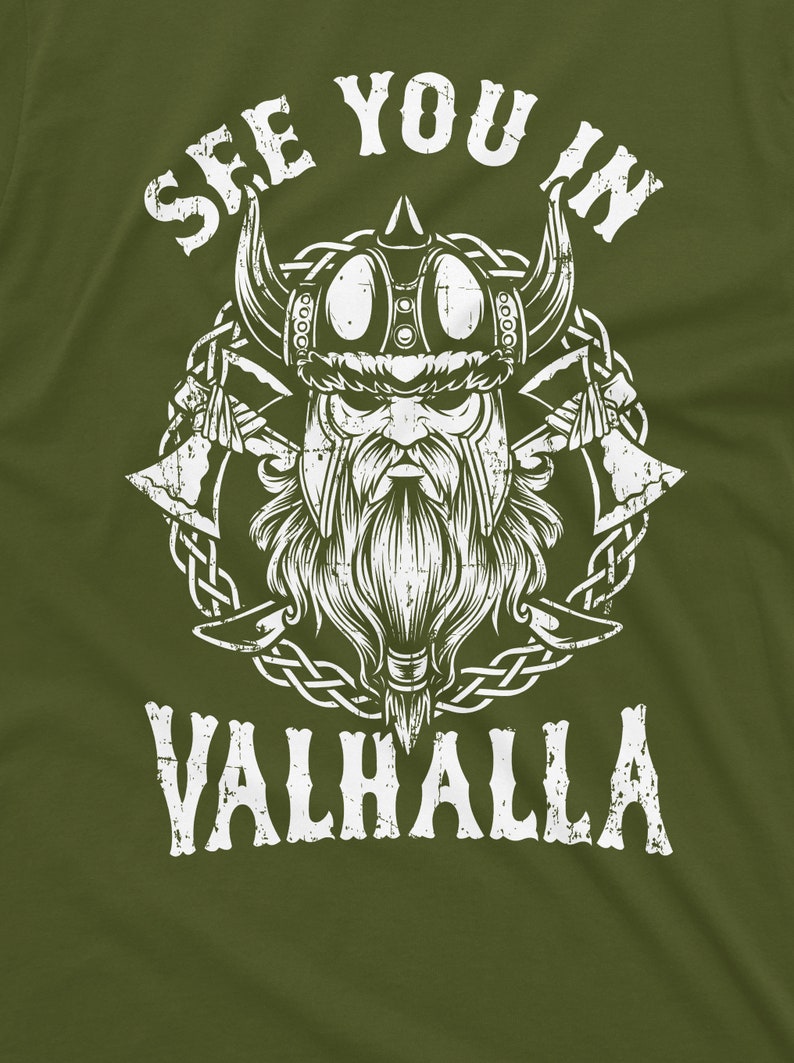 May include: Olive green t-shirt featuring a distressed white graphic of a Viking with a horned helmet, beard, and crossed axes. The text "SEE YOU IN VALHALLA" is arched above and below the Viking illustration.