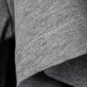 May include: Close-up of a gray t-shirt with a single row of stitching along the seam.