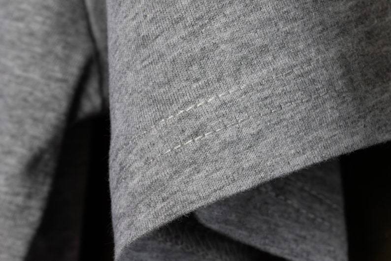 May include: Close-up of a gray t-shirt with a single row of stitching along the seam.