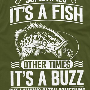 Pu&ograve; includere: Una maglietta verde con un design grafico bianco di un pesce con il testo "Sometimes it's a fish, other times it's a buzz, but I always catch something."