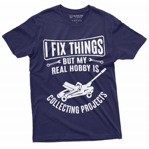 May include: A navy blue t-shirt with white text that reads "I fix things but my real hobby is collecting projects". The text is surrounded by wrench symbols. A white silhouette of a car jack is below the text.