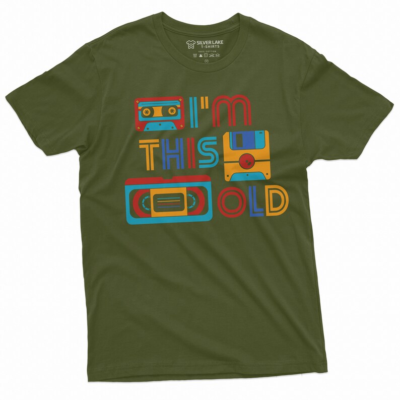 May include: A green t-shirt with a retro design featuring a cassette tape, floppy disk, and VHS tape. The text on the shirt reads "I'm This Old".