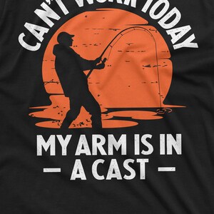May include: A black t-shirt with a white graphic of a silhouette of a person fishing with the text "Can't work today - My arm is in a cast -"