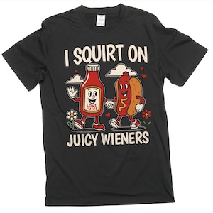 May include: Black t-shirt featuring a cartoon illustration of a ketchup bottle and a hot dog holding hands. The text "I SQUIRT ON JUICY WIENERS" is printed above and below the graphic in white.