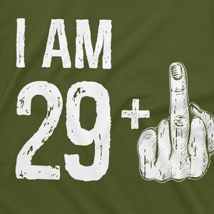 May include: Green t-shirt with white text that says "I AM 29+" and a white hand giving the middle finger.