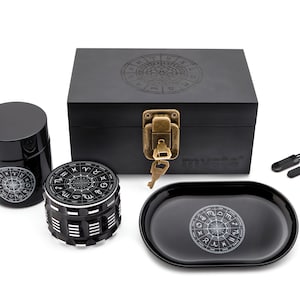 May include: A black wooden box with a lock and key, a black grinder with a zodiac design, a black tray with a zodiac design, and two black tools. The box has the word "myvases" printed on it.