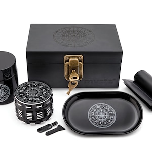 May include: Black wooden box with a lock and key, a black grinder with a zodiac design, a black tray with a zodiac design, and a black rolling tray. The box has the word "mystic" on the front.