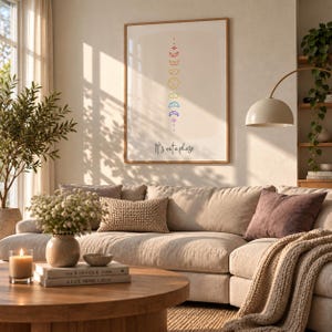 Könnte beinhalten: Ein gerahmter Wandkunstdruck mit einer vertikalen Abfolge von regenbogenfarbenen Mondphasen in einem minimalistischen Stil, zentriert über dem Text "It's not a phase" in schwarzer Schreibschrift, an einer hellen Wand.