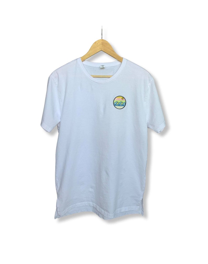 May include: White t-shirt with a small, round, colorful graphic of a sun, waves, and mountains.