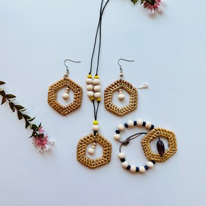 May include: A set of wooden jewelry featuring a necklace, earrings, and a bracelet. The necklace and earrings have a hexagonal shape with a woven design and natural wood beads. The bracelet has a woven design with blue and white beads.