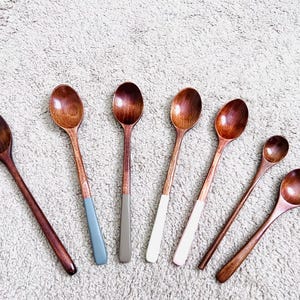 Puede incluir: Siete cucharas de madera con mangos de diferentes colores. Las cucharas son todas de madera natural y tienen un acabado liso. Los mangos están pintados en varios colores, incluyendo azul, gris, rosa y blanco.