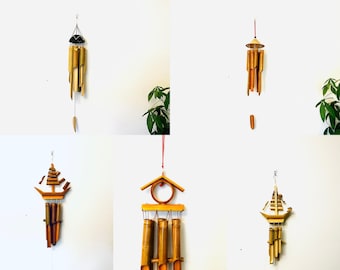 May include: Five different bamboo wind chimes hanging from the ceiling. The wind chimes are made of natural bamboo and have different designs, including a ship, a house, and a simple design with a round top. The wind chimes are all hanging from red strings.