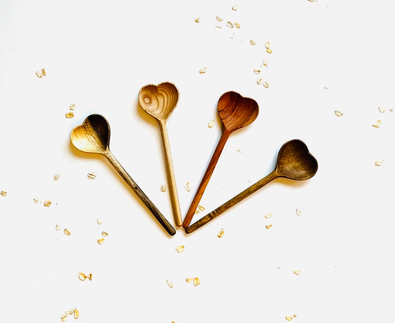 Op de afbeelding: Vier houten hartvormige lepels op een witte achtergrond met gouden confetti. De lepels zijn allemaal in verschillende tinten bruin.
