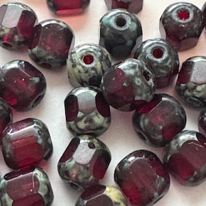May include: Close-up of faceted beads in shades of deep red and gray-green. The beads have a geometric shape with multiple facets, creating a sparkling effect. These beads are suitable for jewelry making and crafting.
