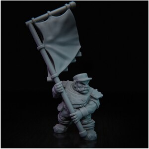 May include: A gray plastic miniature figurine of a soldier holding a flag. The soldier is wearing a hat and has a beard. The flag is plain and gray.