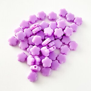 K&ouml;nnte beinhalten: Ein Haufen violetter, blumenf&ouml;rmiger Plastikperlen. Die Perlen haben ein Loch in der Mitte zum Auf f&auml;deln.