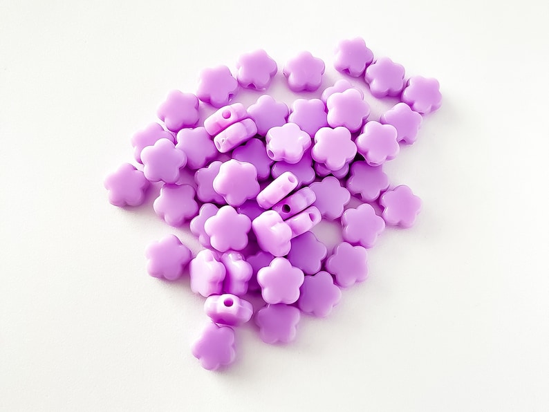 K&ouml;nnte beinhalten: Ein Haufen violetter, blumenf&ouml;rmiger Plastikperlen. Die Perlen haben ein Loch in der Mitte zum Auf f&auml;deln.