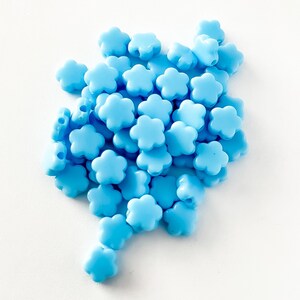 K&ouml;nnte beinhalten: Ein Haufen hellblauer, blumenf&ouml;rmiger Perlen. Die Perlen sind aus Kunststoff und haben eine glatte Oberfl&auml;che.